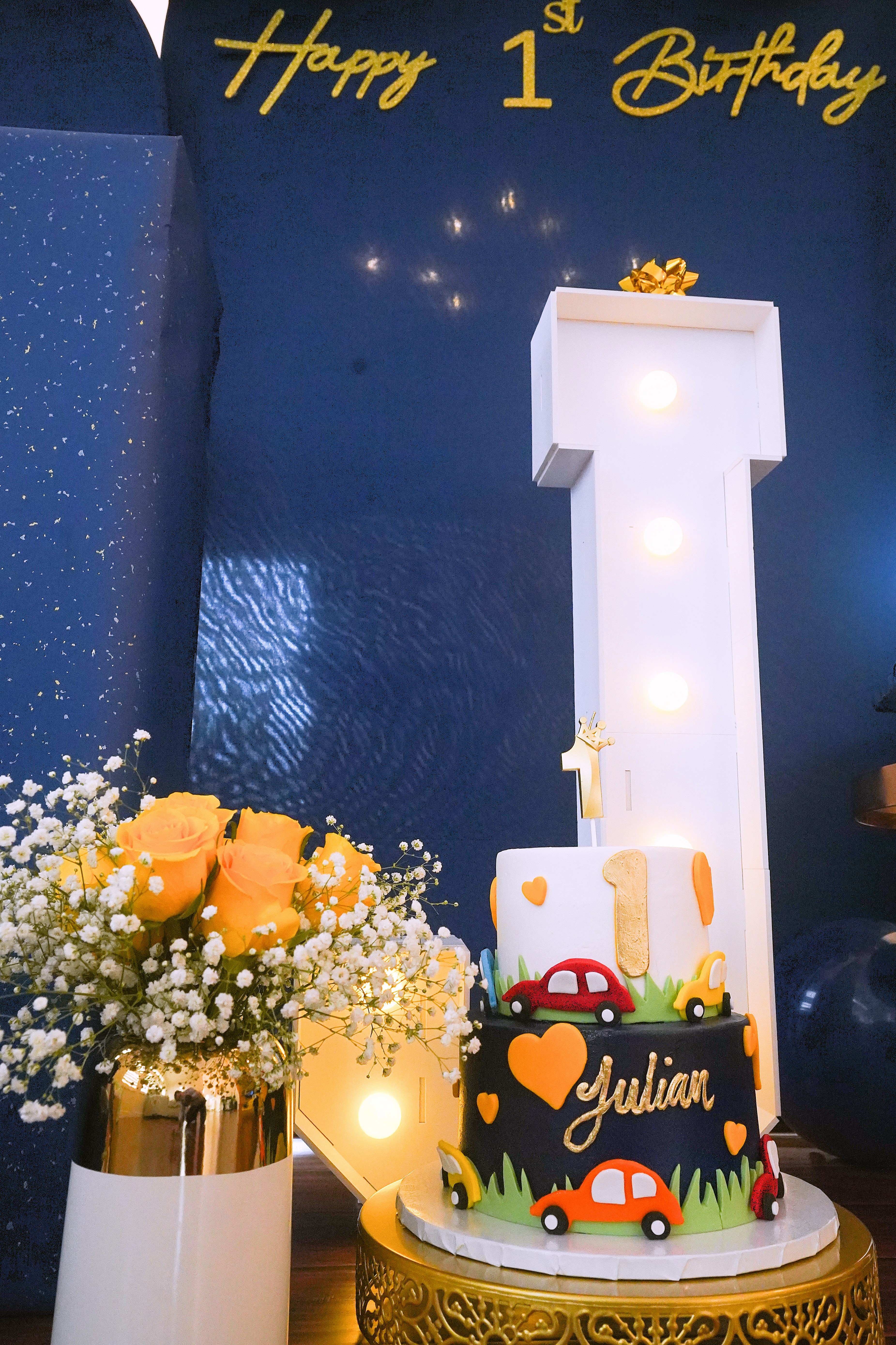 Personalized first birthday cake with colorful cars, yellow roses, and an illuminated number one