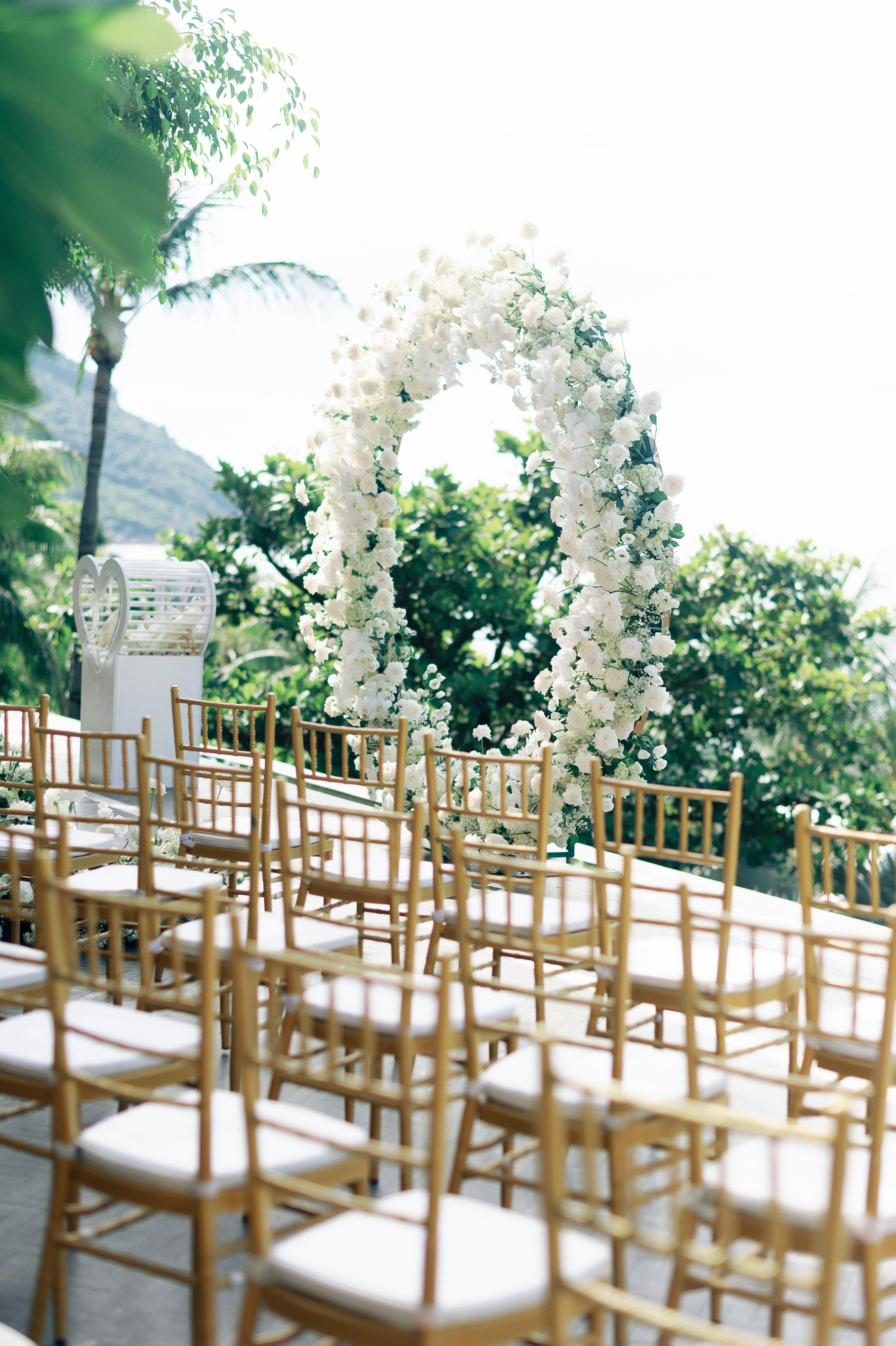 White floral wedding arch with gold chairs at an outdoor ceremony